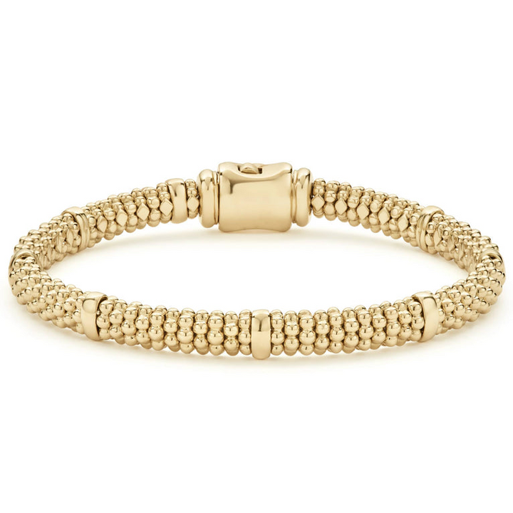 An 18k gold bracelet resting in the middle of a white background. The bracelet features smooth stations, caviar beading, and gold clasp.