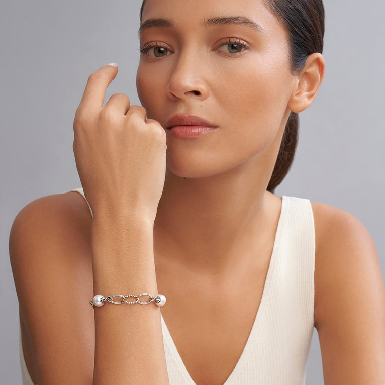 A close-up of a woman wearing a Sterling Silver link bracelet rests in the middle of a white background. It has three cultured freshwater pearl stations and caviar-beaded links.