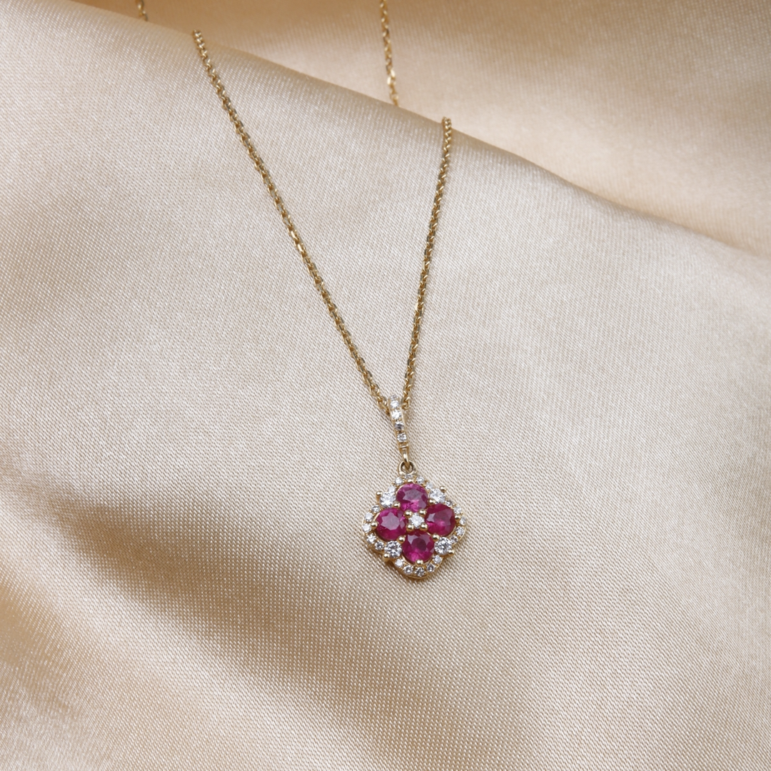 A close-up of a yellow-gold Halo Clover Necklace against a gold background. The necklace features a clover motif pendant with ruby round diamonds, milgrain detailing, and a 14k yellow gold chain.