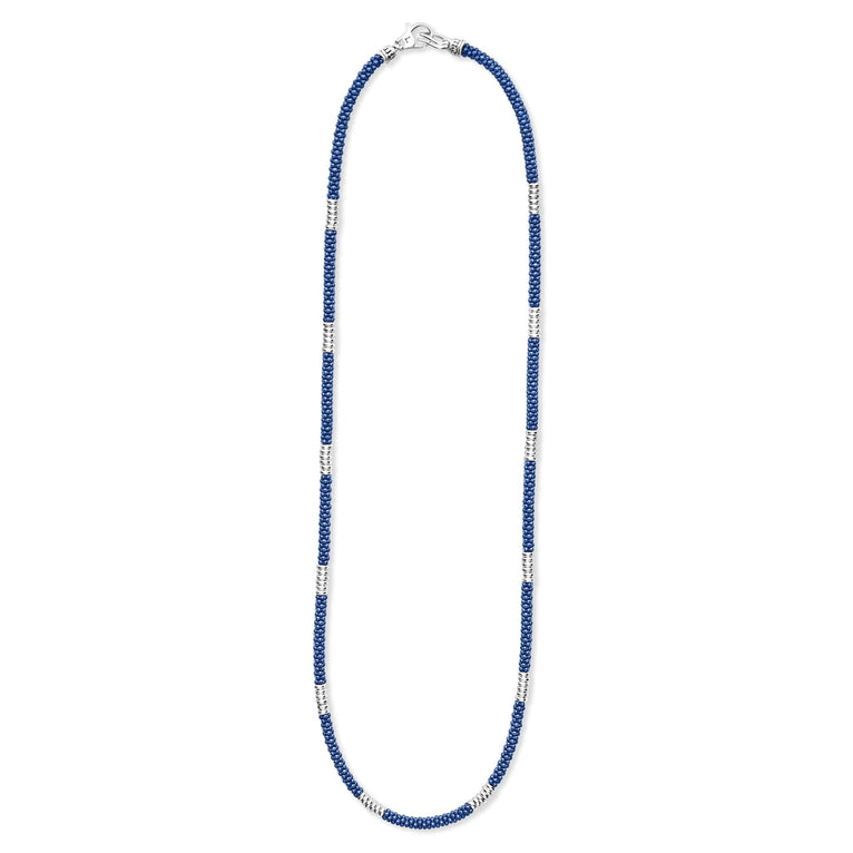 A sterling silver and ceramic beaded necklace in the middle of a white background featuring blue ceramic and silver Caviar beading.