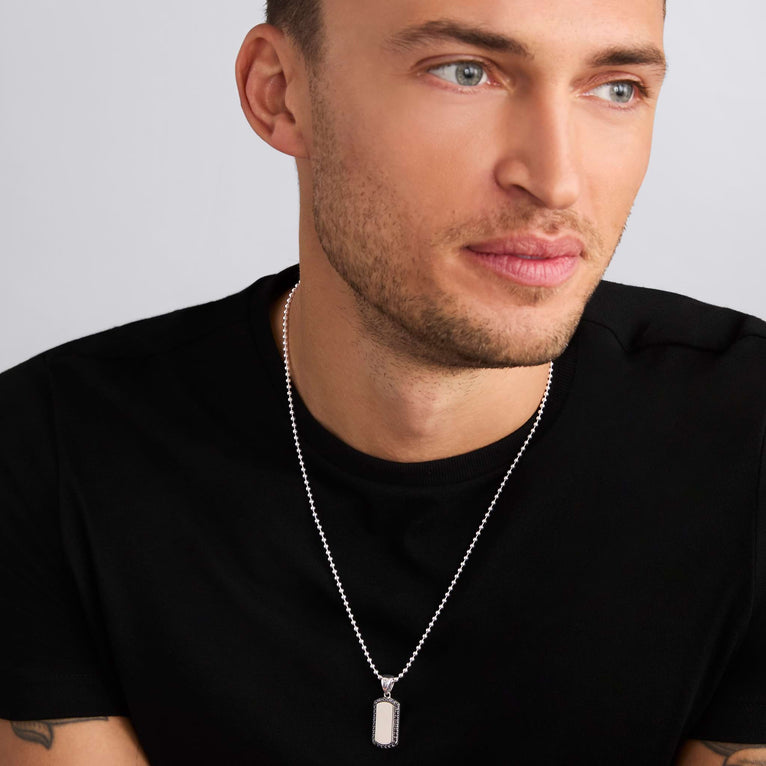 A man is wearing a sterling silver amulet featuring black diamonds accented by smooth silver and Caviar beading