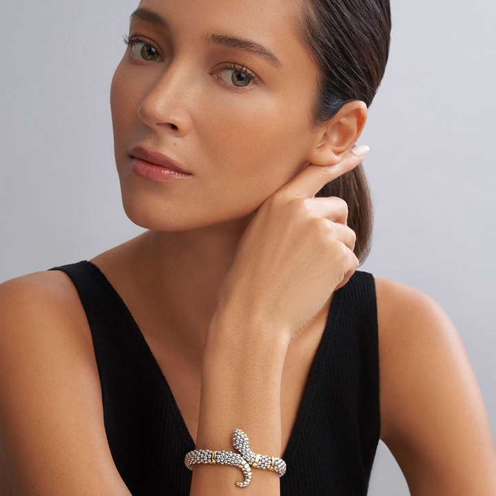 A woman wearing a sterling silver & 18k gold bracelet in the middle of a white background featuring a snake motif, gold stations, and sterling silver caviar beading.