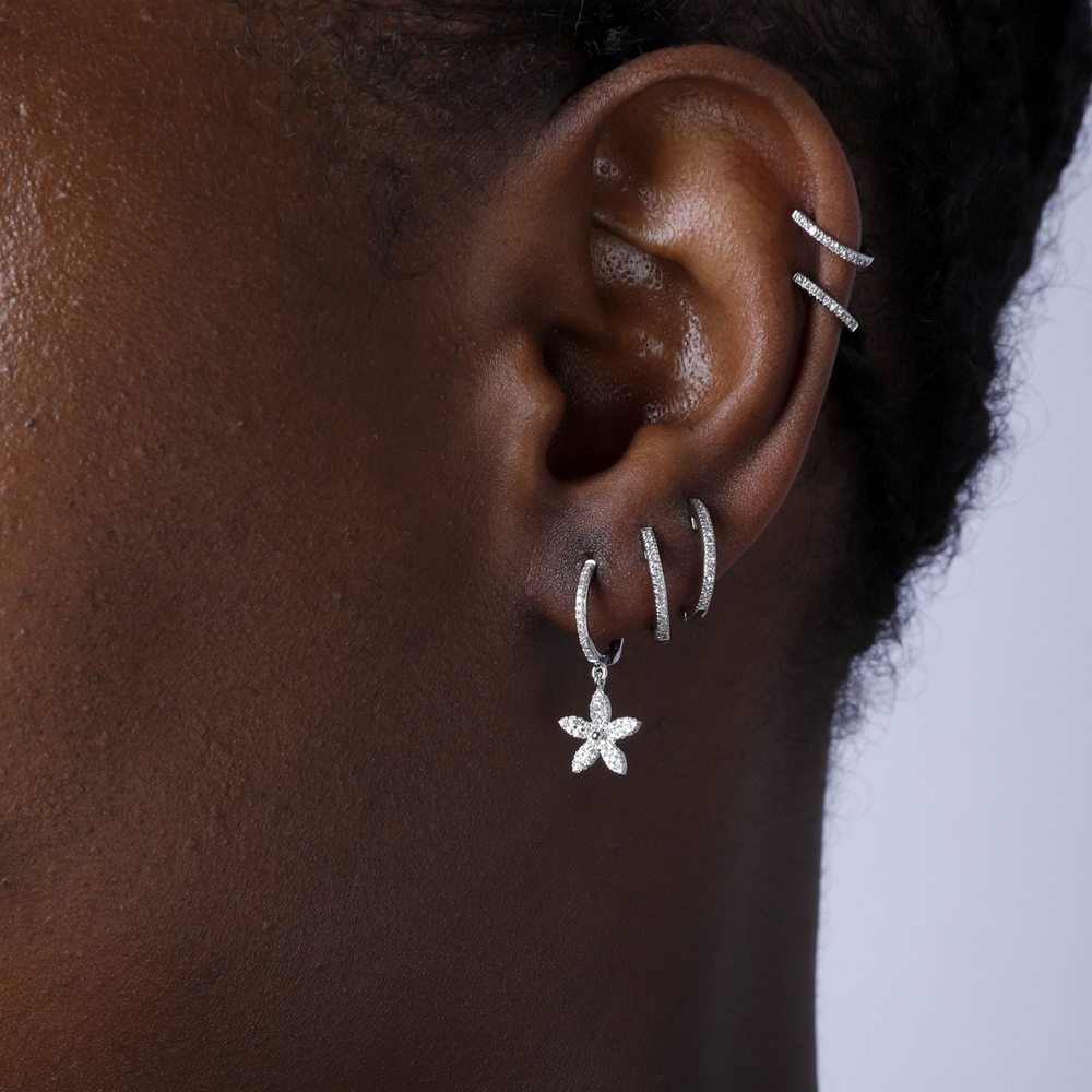 A woman with short black hair is wearing a pair of drop diamond earrings. The earrings have a flower design and a cluster of diamonds.