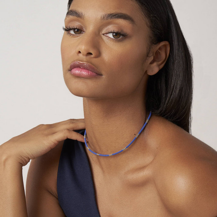 A woman wearing a sterling silver and ceramic beaded necklace featuring blue ceramic and silver Caviar beading.