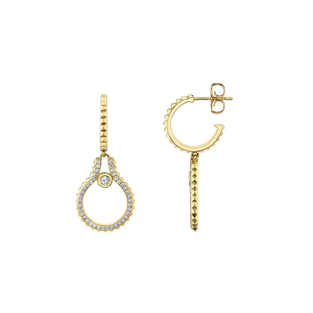 Two yellow-gold earrings are lying flat against a white background. The earrings feature bezel-set diamonds on a namesake pendant.