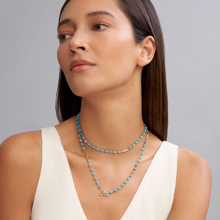 A woman is wearing a sterling silver and ceramic beaded necklace featuring turquoise ceramic and silver caviar beading.