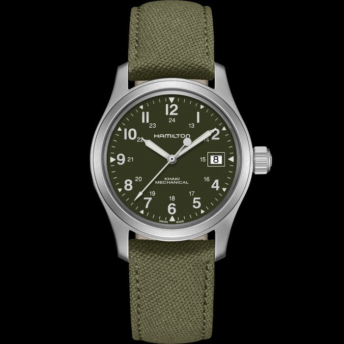 A Hamilton watch is laid out against a black background. It features a green dial, white hands and markers, a stainless steel case, a steel bezel, a steel crown, and a green canvas strap.