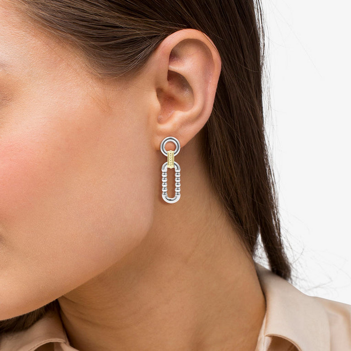 A woman wearing a button down and a pair of link drop earrings with Sterling silver and 18k gold variations of Caviar beading and fluting elements. 