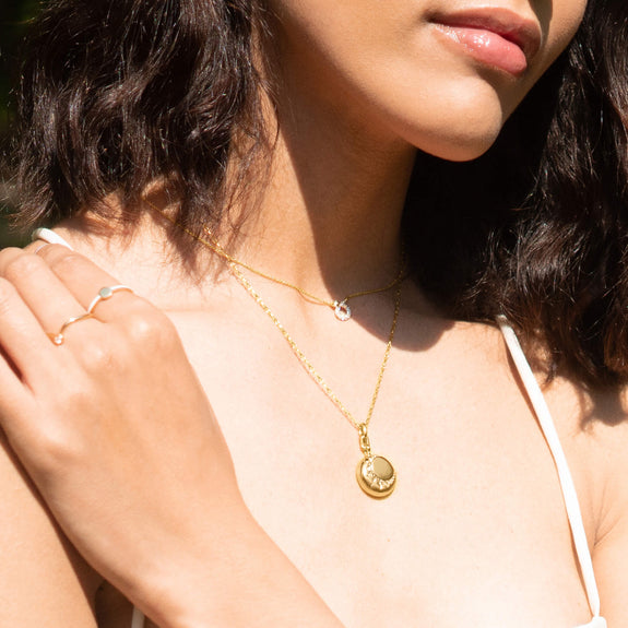 A woman wearing a Gold Locket necklace set with White Diamonds, a sun motif, and a gold chain