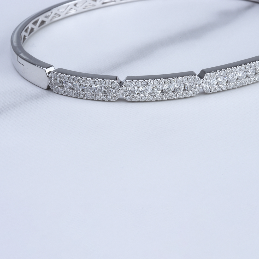 A close-up of a 14k white gold bangle bracelet features a pave diamond cluster design on top of a white cloth.