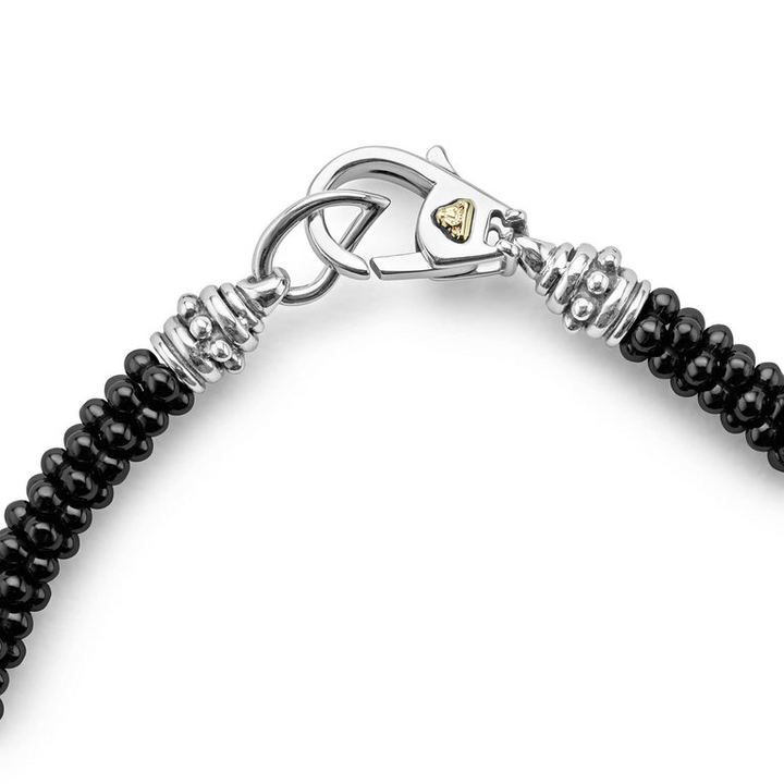 A sterling silver & 18k gold bracelet focusing on the clasp of a white background featuring five sterling silver stations and black ceramic caviar beading.