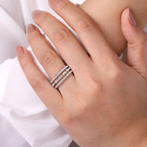 A close-up of a woman wearing a white gold ring on her ring finger. The ring features a three-row design with two outer bands featuring straight strands of glittering pavé diamonds, while the central row of diamonds is sculpted into a series of elegant marquise shapes.