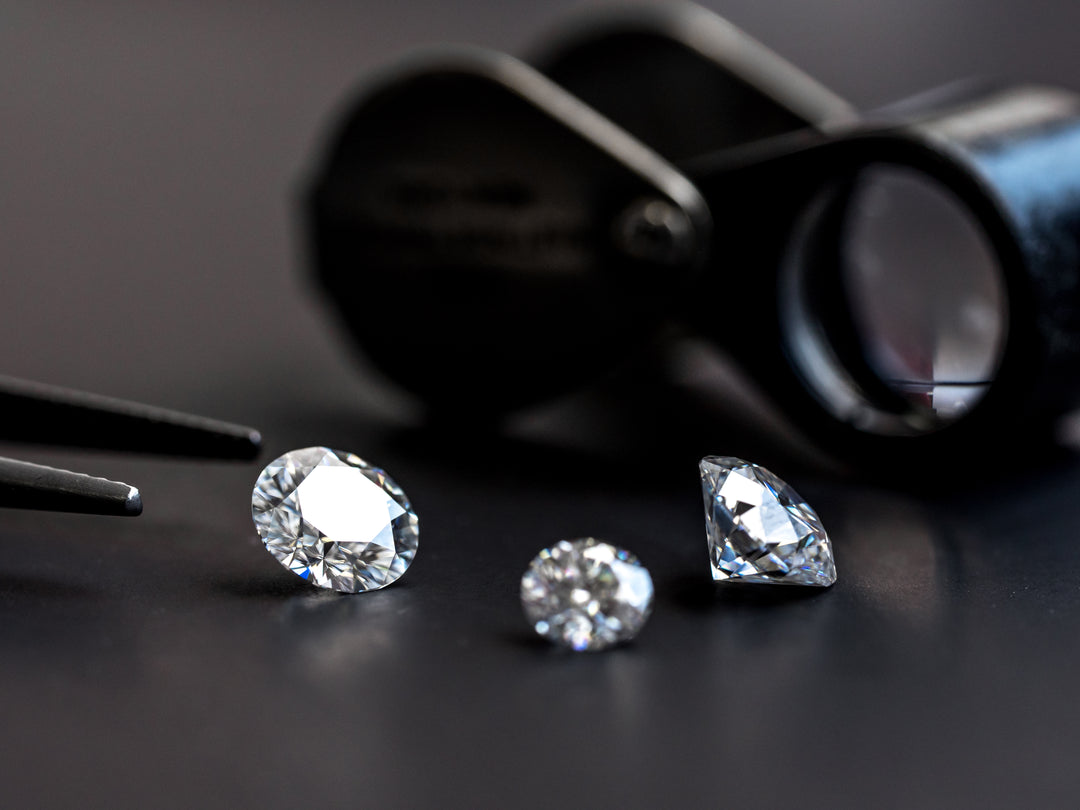 photo of 3 loose diamonds sitting on a black surface with a pair of tweezers appearing to the left of the loose diamonds