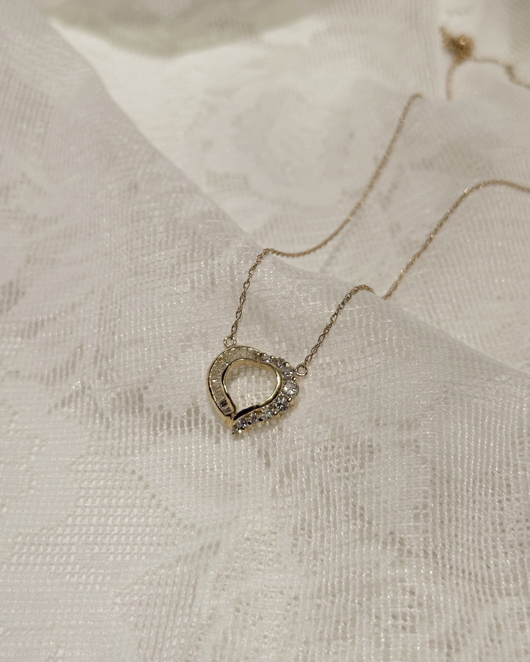 14K yellow gold diamond heart pendant necklace draped over a white patterned cloth.