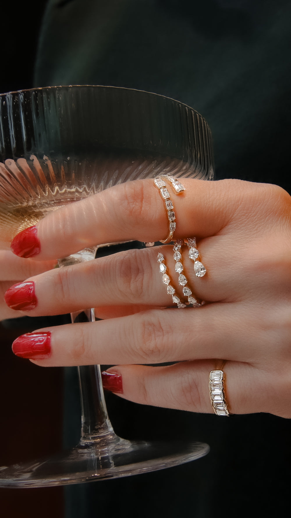 A close-up of a woman's hand, with red fingernail polish, features a yellow gold diamond ring on her ring finger. The ring features pear-shaped diamonds set in lustrous yellow gold and a three-row wrap design.