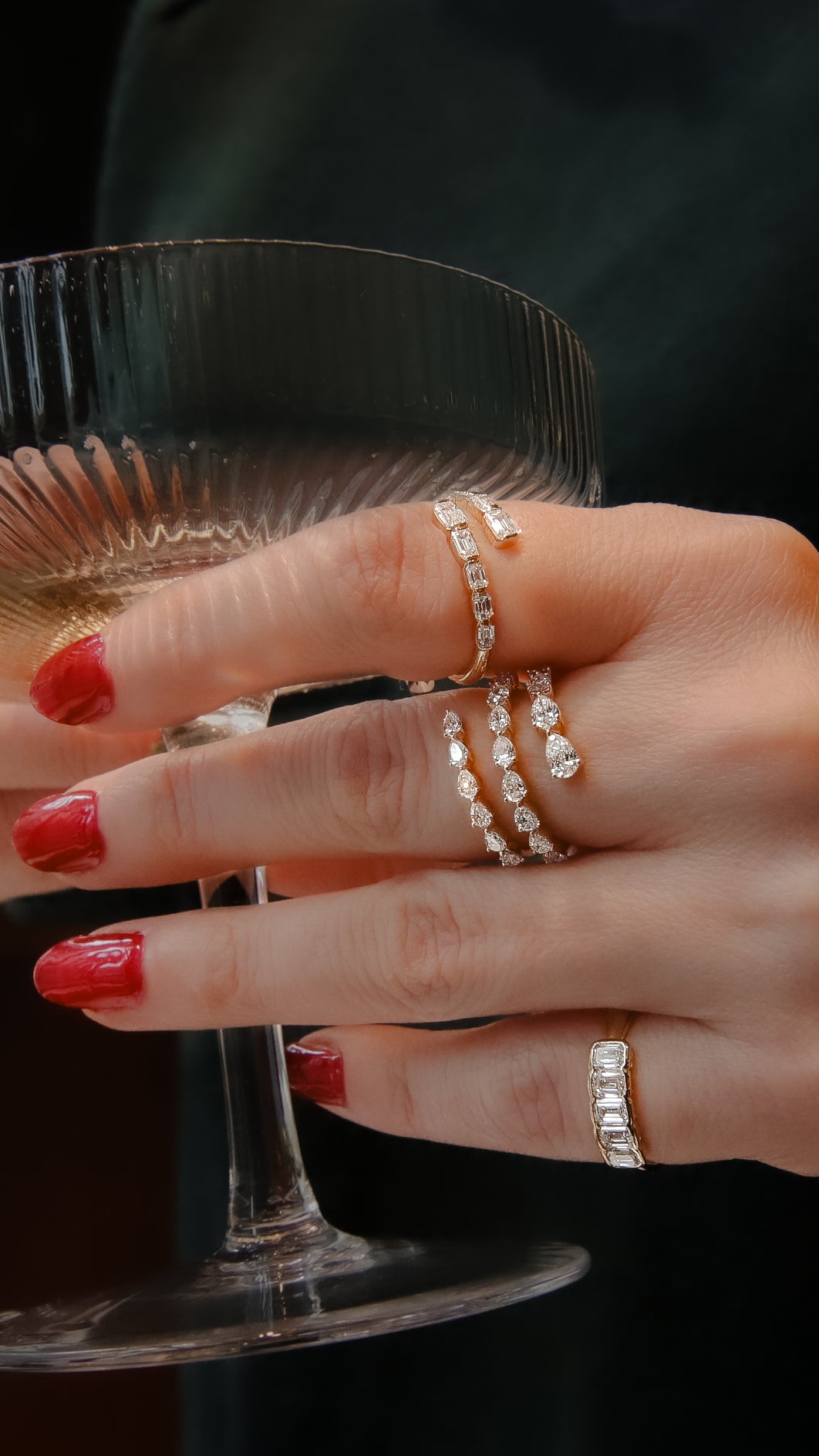 A close-up of a woman's hand, with red fingernail polish, features a yellow gold diamond ring on her ring finger. The ring features pear-shaped diamonds set in lustrous yellow gold and a three-row wrap design.