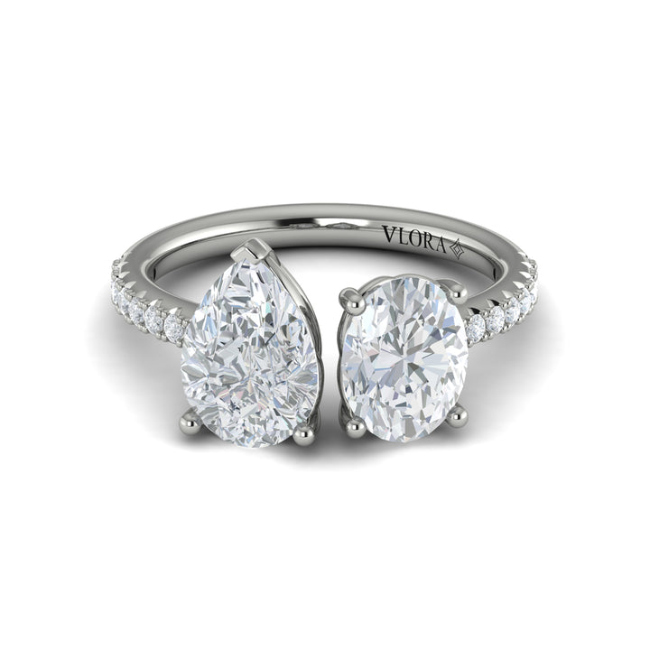 A front view of a white gold engagement ring is set against a white background. The engagement ring features an oval and pear-shaped diamond meeting in the center, surrounded by a half-eternity diamond band.