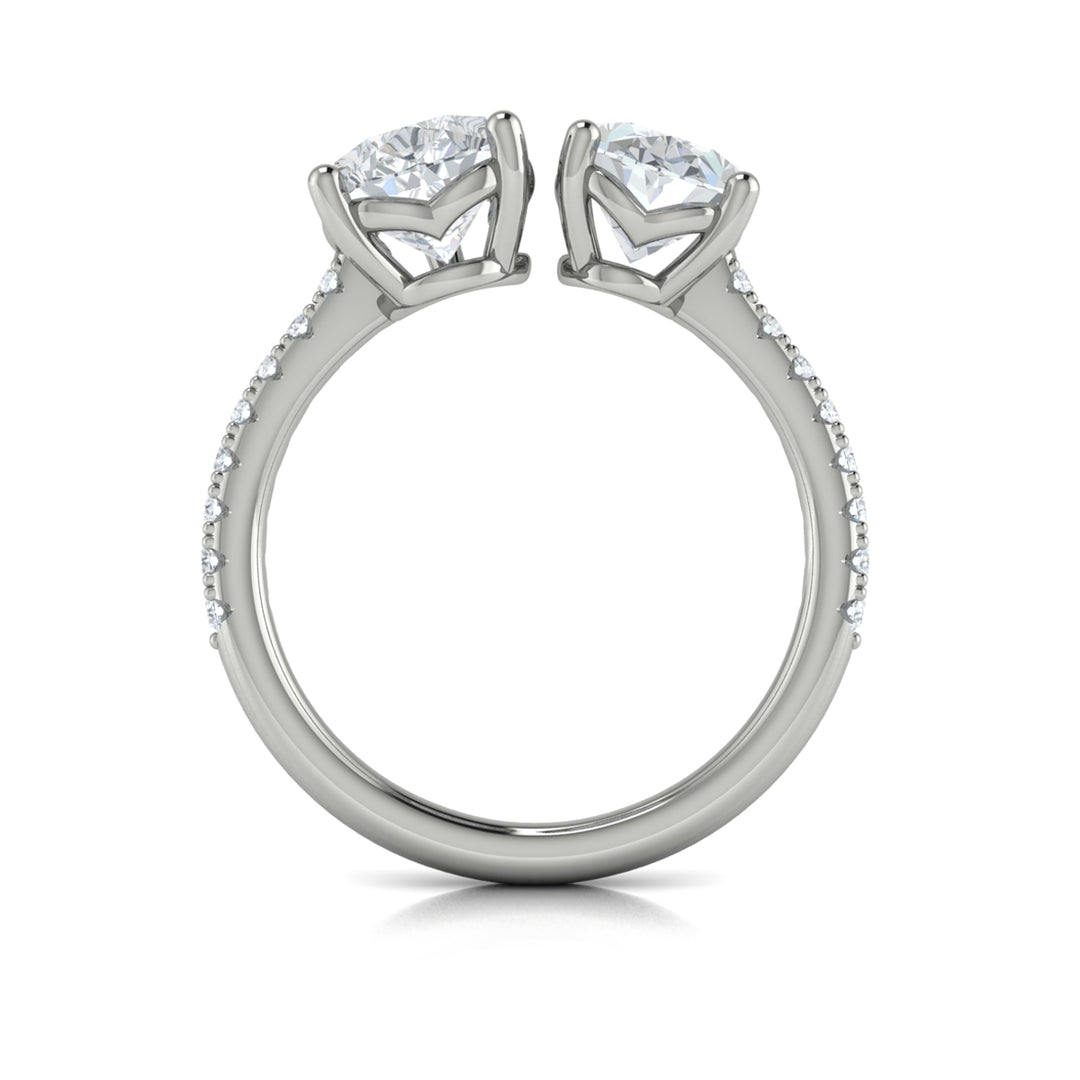 A top view of a white gold engagement ring is set against a white background. The engagement ring features an oval and pear-shaped diamond meeting in the center, surrounded by a half-eternity diamond band.