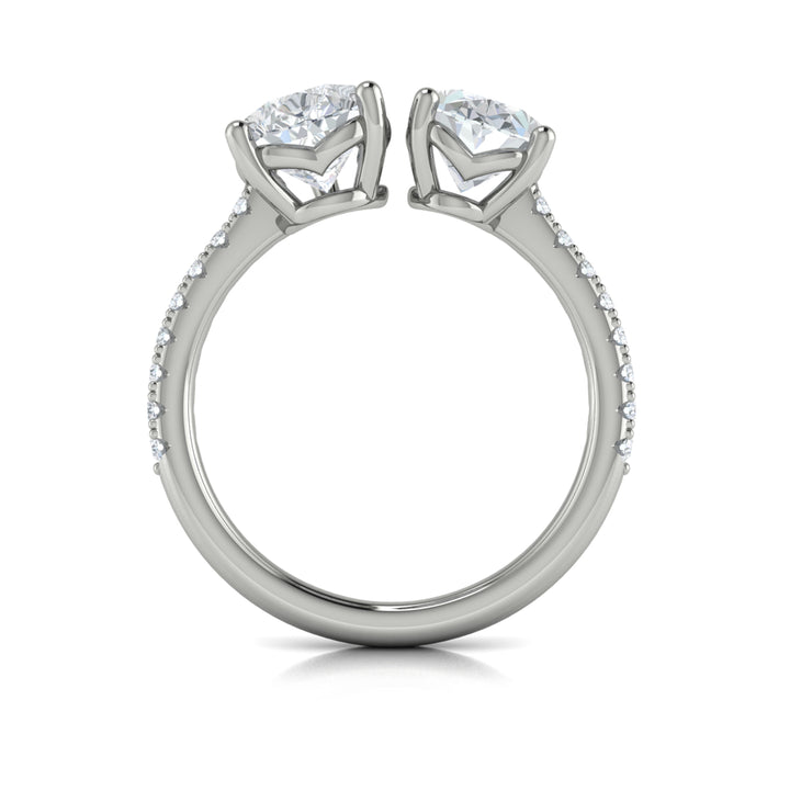A top view of a white gold engagement ring is set against a white background. The engagement ring features an oval and pear-shaped diamond meeting in the center, surrounded by a half-eternity diamond band.