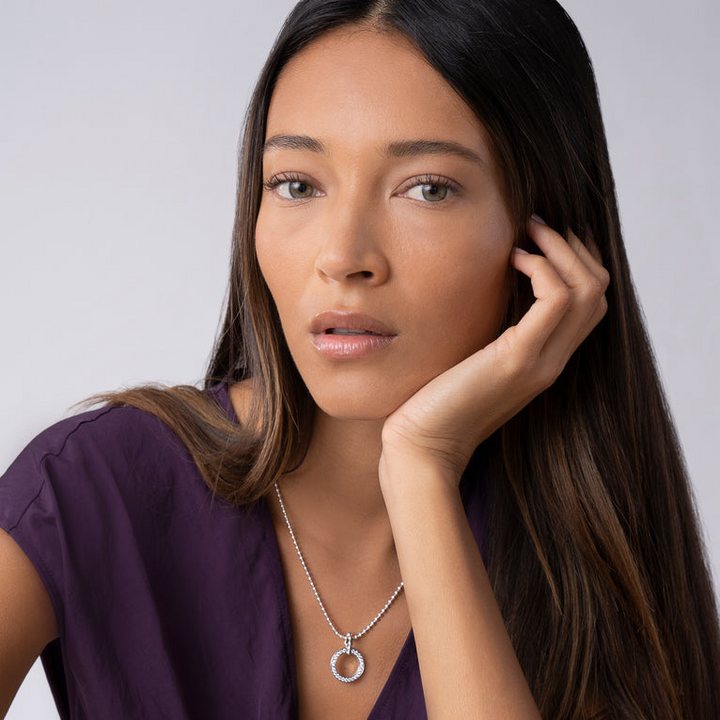 A close-up of a woman wearing a sterling silver necklace featuring a diamond circle pendant against a white background.