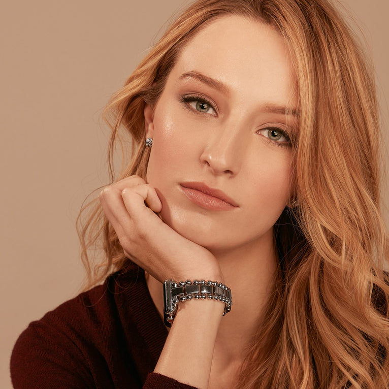 A woman is wearing a black long-sleeve top, watch, and sterling silver stud earrings with classic caviar beads. 