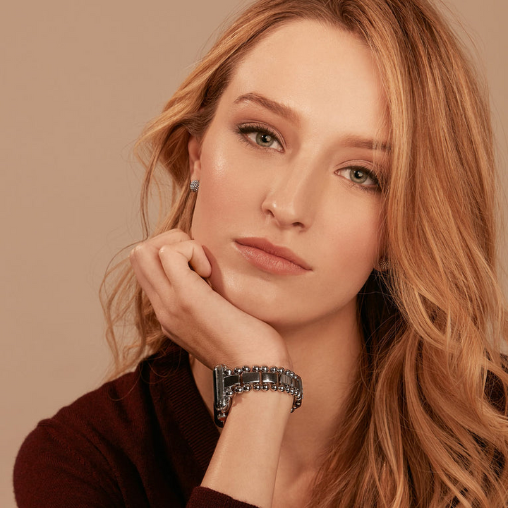 A woman is wearing a black long-sleeve top, watch, and sterling silver stud earrings with classic caviar beads. 