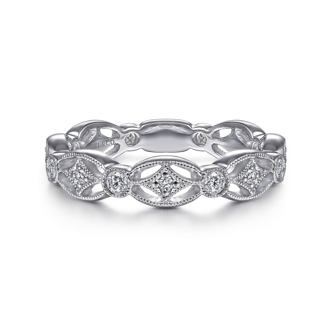 A white gold ring lies flat against a white background. The band features a cutout design with diamond stations.