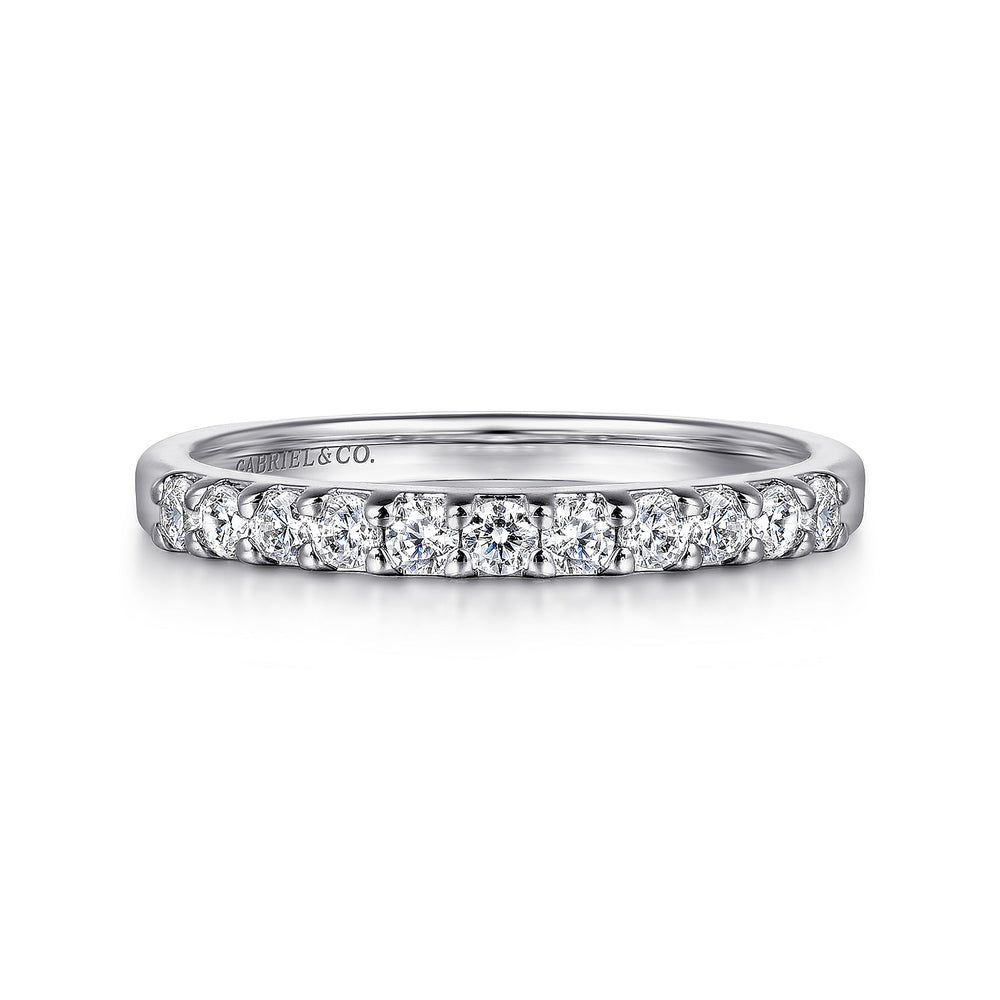 A white gold ring lies flat against a white background. The band features eleven round-cut diamonds in a straight line.