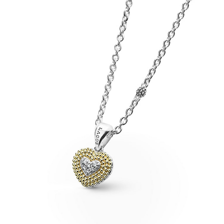 A close-up of a sterling silver &18k gold necklace angled to the right featuring a diamond heart pendant framed by 18K Gold Caviar beadings accented against a white background.