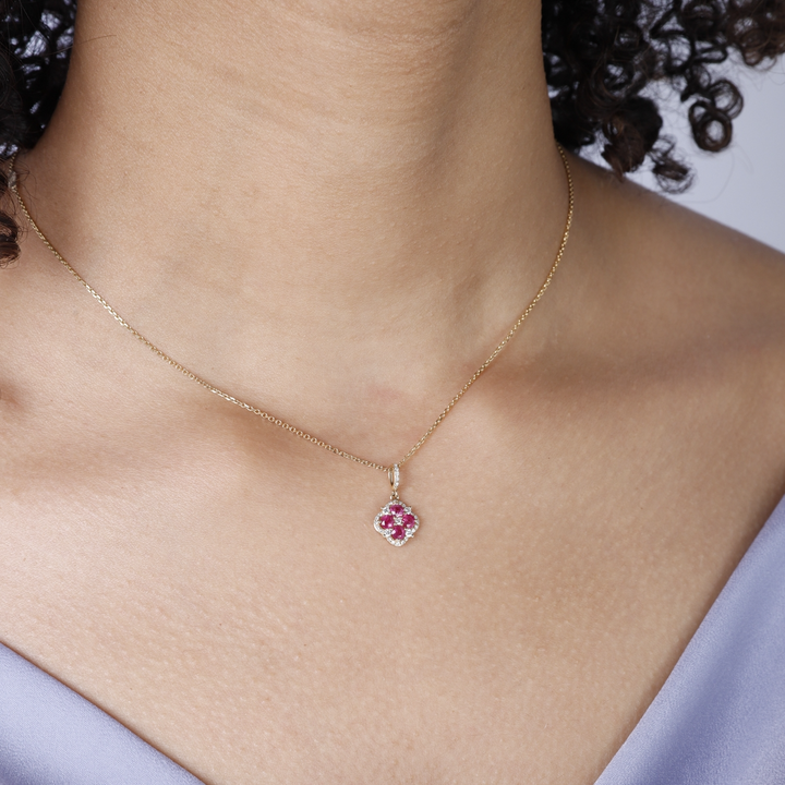 A woman is wearing a yellow-gold Halo Clover Necklace and a purple top. The necklace features a clover motif pendant with ruby round diamonds, milgrain detailing, and a 14k yellow gold chain.