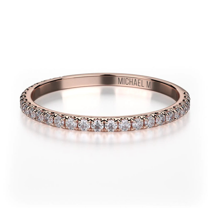 A rose-gold ring lies flat against a white background. It features a bezel set of round diamonds, and the "Michael M" inscription is visible inside it.