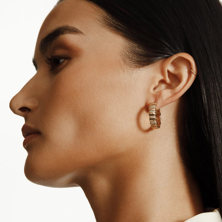 A close-up of a woman wearing a yellow-gold earring. The hoop earrings feature pave-set round diamond stations.