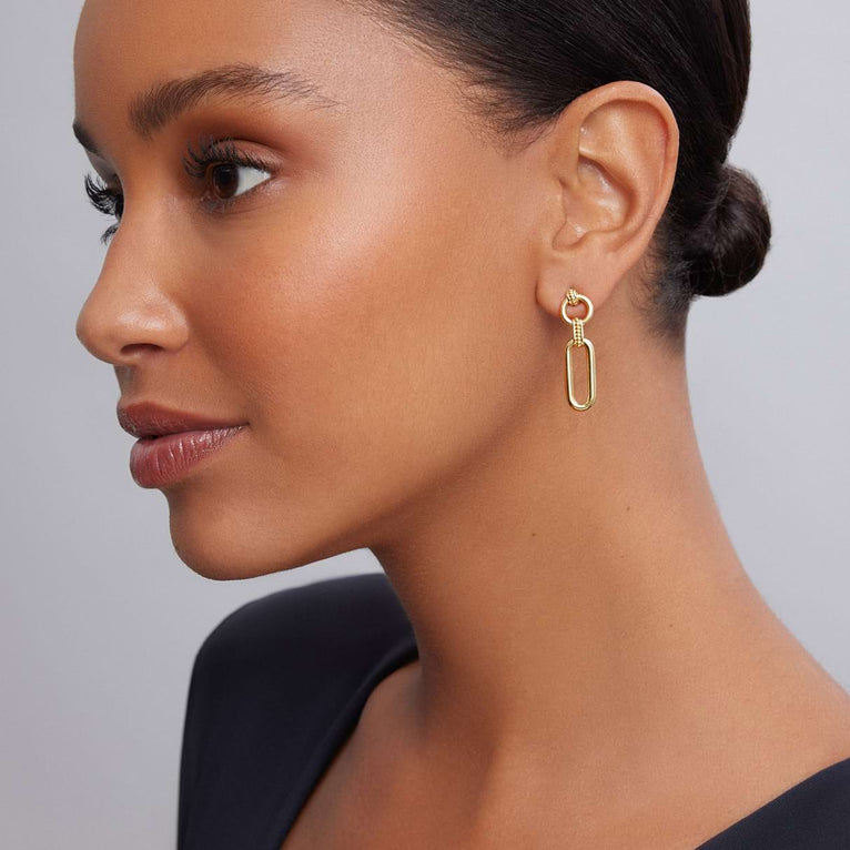 A woman wearing a black shirt and 18K gold variations of Caviar beading & fluting elements link drop earrings