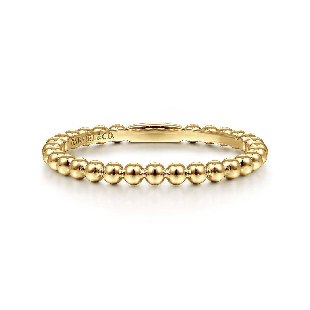 A yellow-gold ring lies flat against a white background. The band features yellow-gold beads.