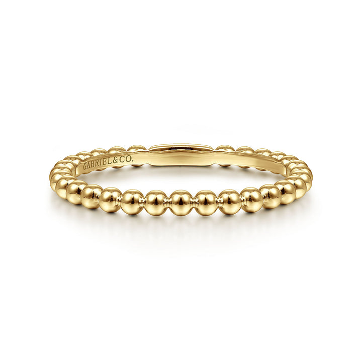 A yellow-gold ring lies flat against a white background. The band features yellow-gold beads.