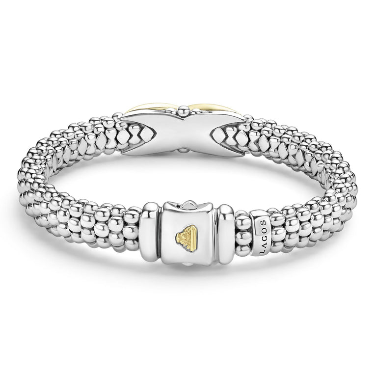 A Sterling Silver & 18k gold bracelet resting in the middle of a white background highlighting the clasp. The bracelet features a gold X station, caviar beading, and a stainless steel clasp.