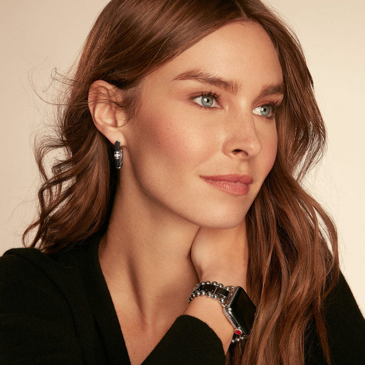 A woman wearing a black top, an apple watch, and a pair of hoop earrings with Black ceramic Caviar beading, sterling silver, and diamonds.