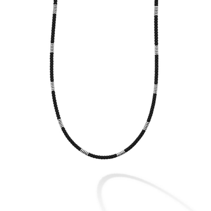 A close-up of a sterling silver and ceramic beaded necklace in the middle of a white background featuring matte black ceramic and silver Caviar beading.