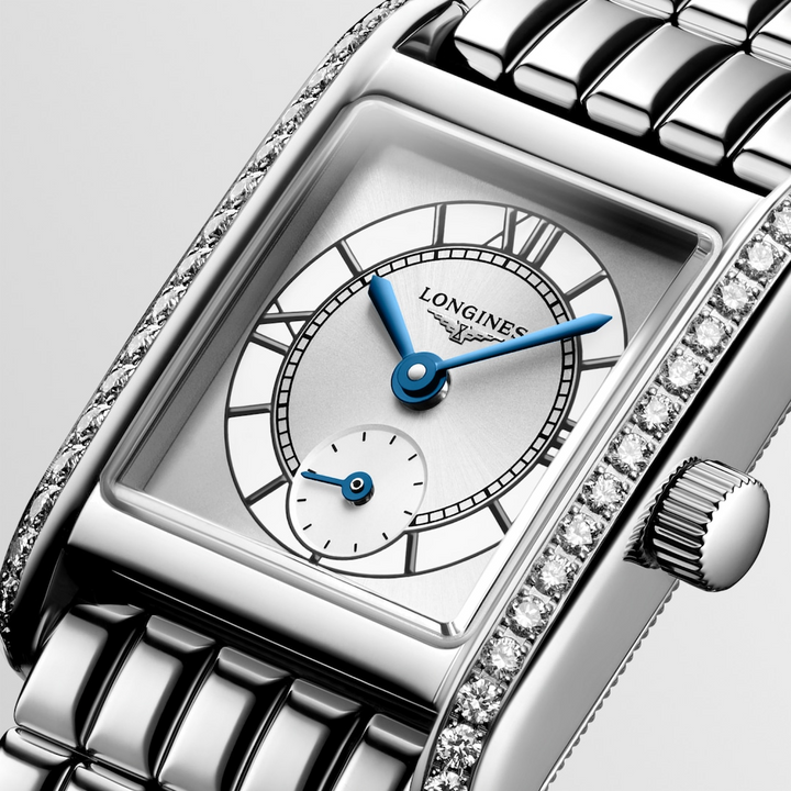 This is a close-up of a Longies watch angled to the right, showcasing the dial with a white background. The rectangular-shaped watch features a white dial, blue hands, black markers, a stainless steel diamond-set bezel, and a stainless steel bracelet.