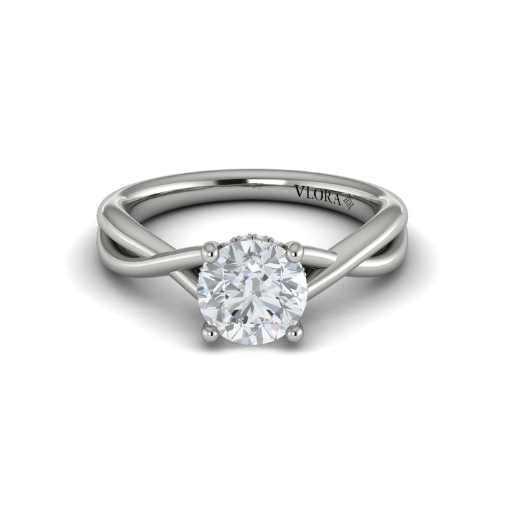 A front view of a white gold engagement ring is set against a white background. The engagement ring features a round center diamond, a cathedral setting, a hidden halo, and a twisted band design.