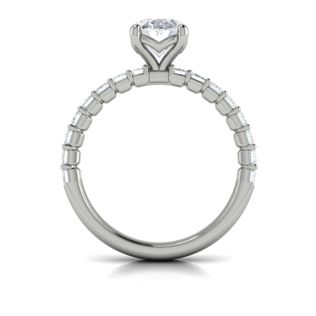 A top view of a white gold engagement ring is set against a white background. The engagement ring features an oval-shaped center stone, raised in the Vlora signature V-setting, with emerald-cut accent diamonds blazing across the band.
