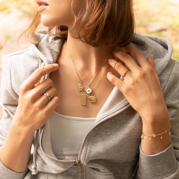 A woman is wearing a gray sweatshirt and multiple gold lockets with a diamond in the center.