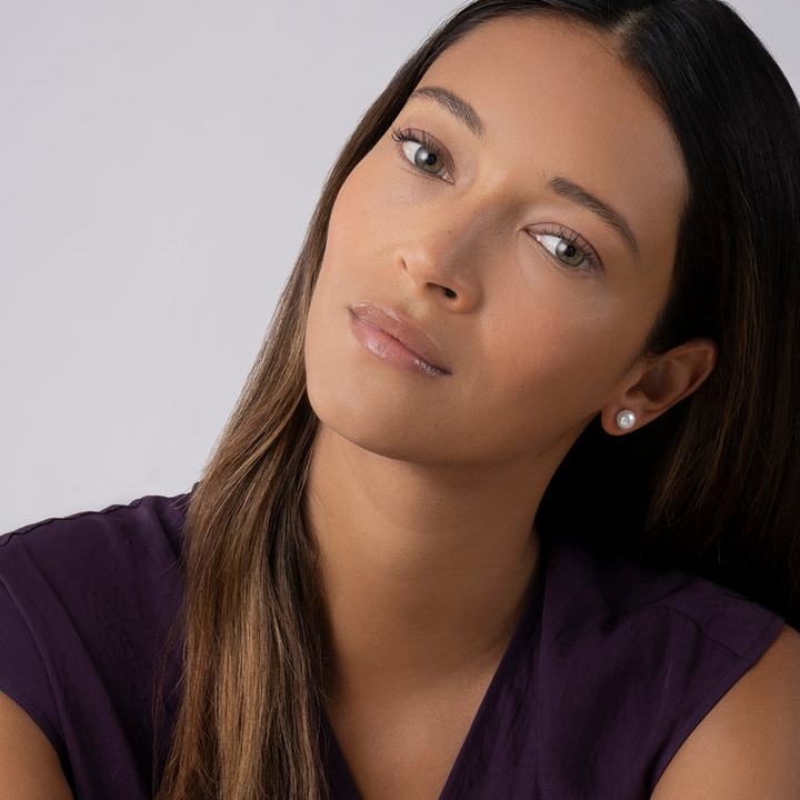 A woman wearing a black shirt and a pair of stud earrings with a cultured freshwater pearl framed by flutes of sterling silver. 