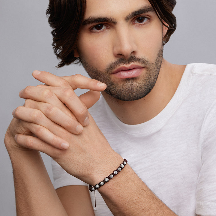 A man is wearing a brown bracelet featuring braided nylon with sterling silver Caviar beads.