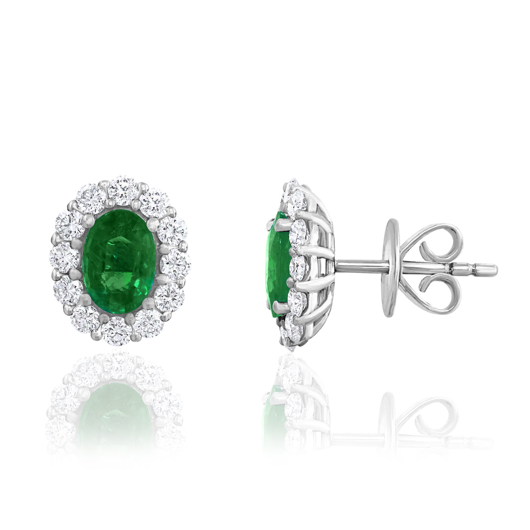 A pair of stud earrings displayed in the middle of a white background, the right earring angled to the side. The earring features an emerald center stone with surrounding diamonds.