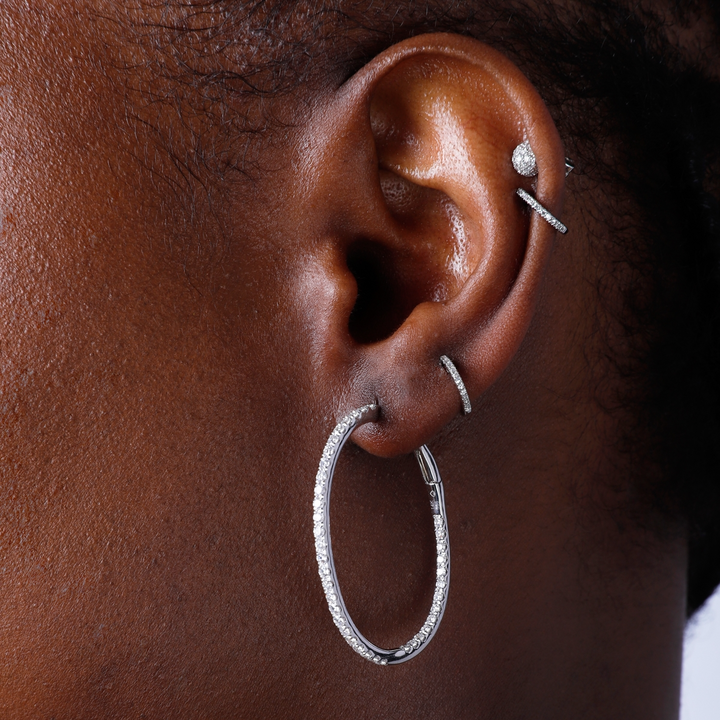 A woman with short black hair is wearing a pair of hoop earrings with a single row of round diamonds. 