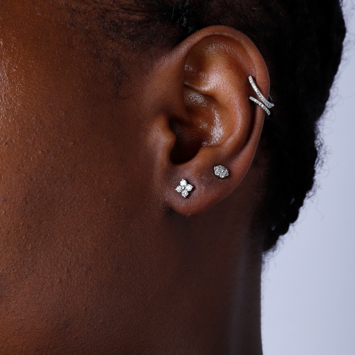 A woman with long black hair is wearing a pair of stud earrings with a flower design and round diamond clusters.