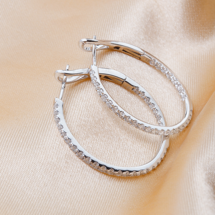 A pair of white gold hoop earrings with a single row of round diamonds resting against a gold background.