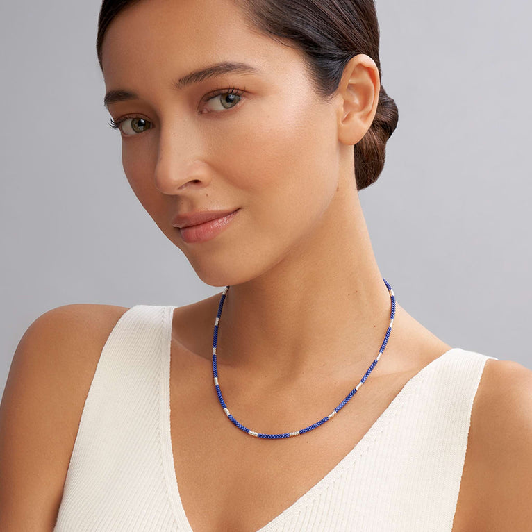 A woman wearing a sterling silver and ceramic beaded necklace featuring blue ceramic and silver Caviar beading.