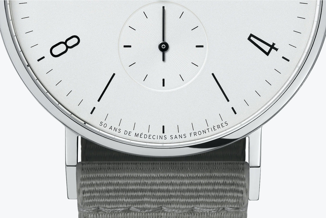 This is a close-up image of a Nomos Glashutte watch, focusing on the dial. It features a white dial, black hands and markers, a stainless steel bezel, and a gray strap.